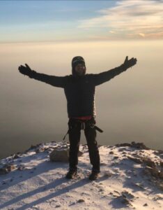 Nolan Tatro arms wide open over the clouds hiking the mountain top